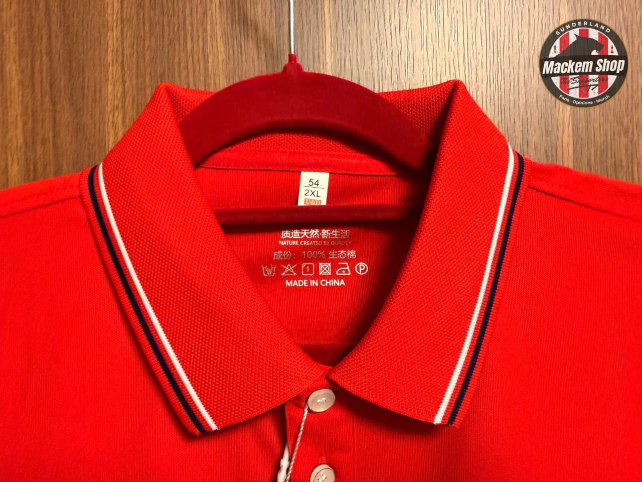 Red polo shirt with white collar and black trim on a wooden background
