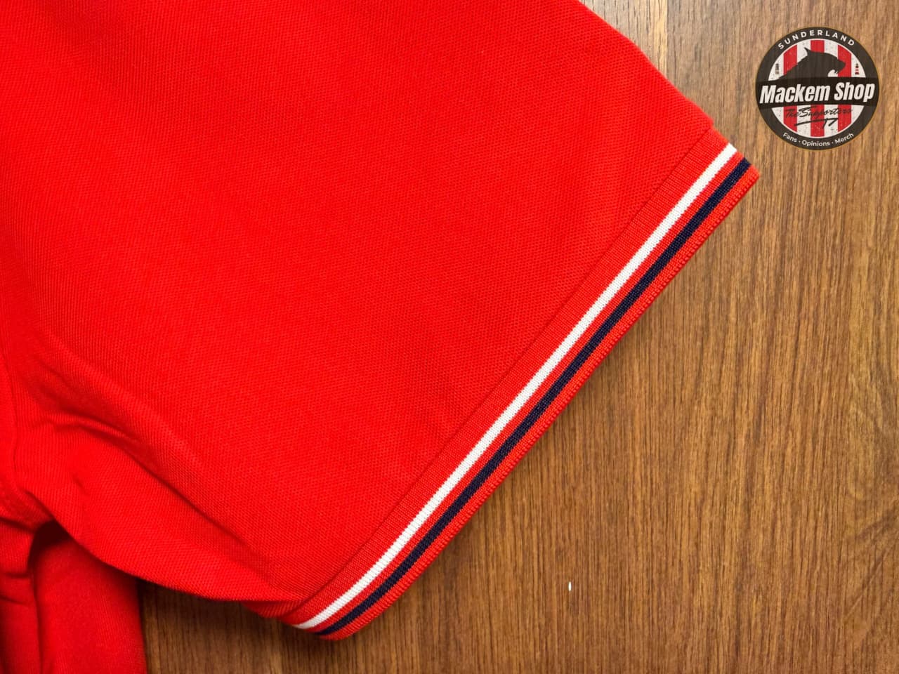 Red garment with white and navy trim on a wooden surface, featuring a logo in the corner.