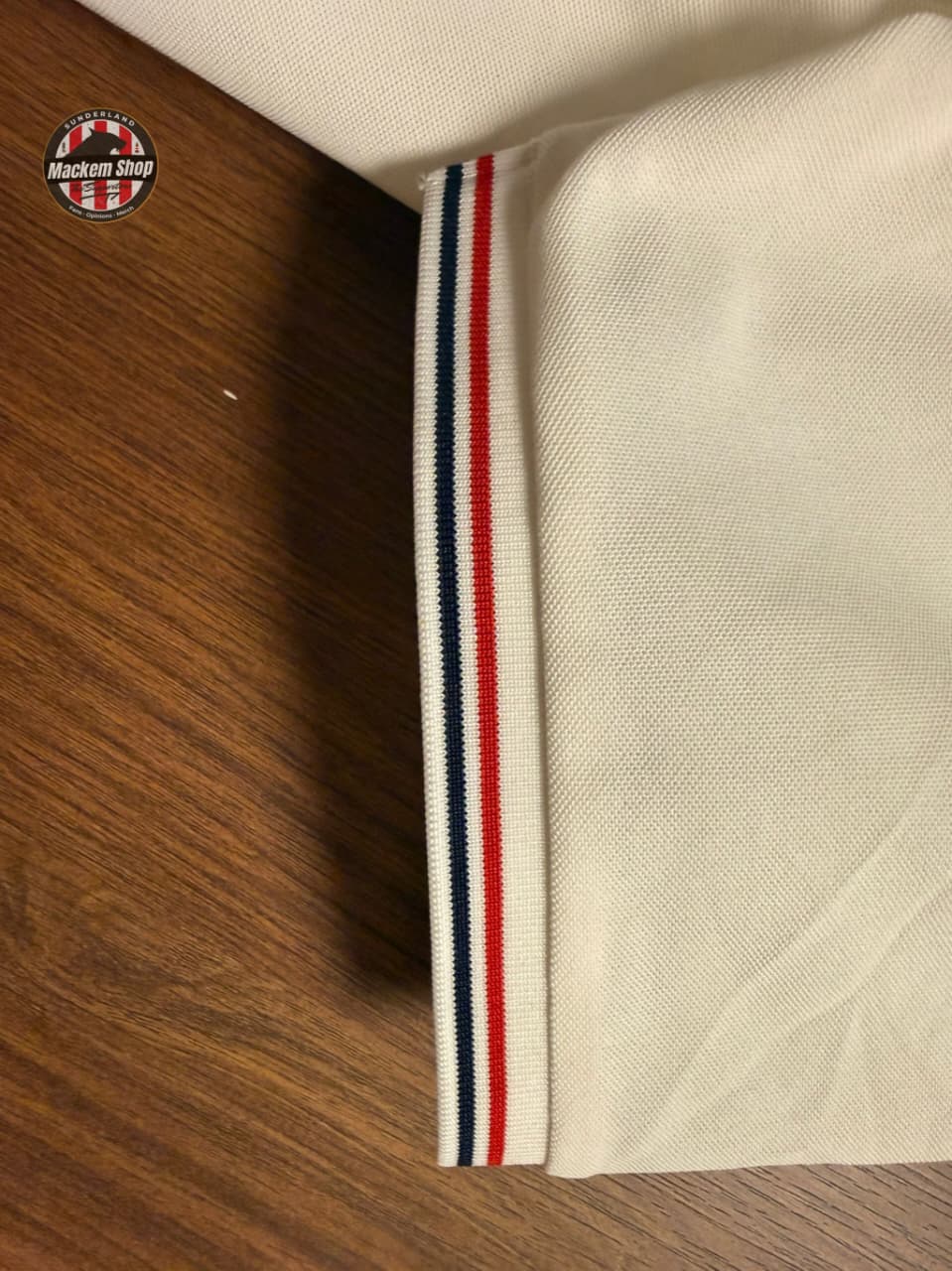 Close-up of beige fabric with a striped trim on a wooden surface, featuring the 'Macken Shop' logo.
