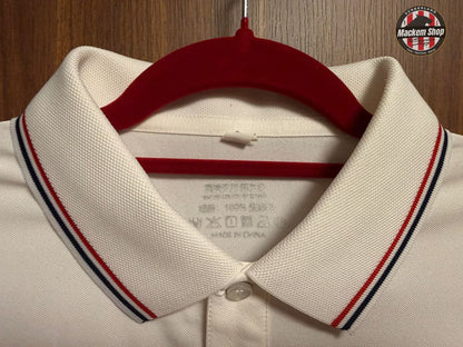 White polo shirt with red, blue, and black striped collar on a hanger against a wooden background.