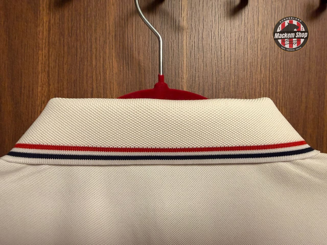 Beige shirt with red, white, and blue stripes on a hanger against a wooden background.