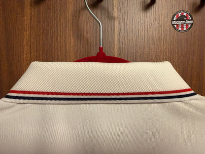Beige shirt with red, white, and blue stripes on a hanger against a wooden background.
