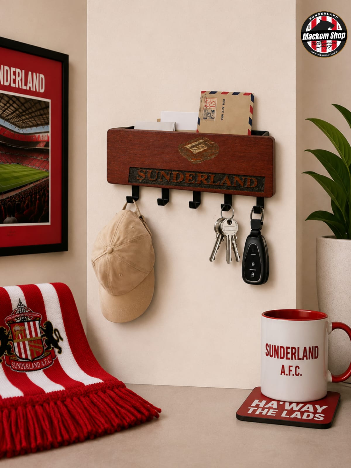 A wooden wall-mounted mail holder and coat rack with black hooks, shown in a styled room setting. The rack is branded with 'SUNDERLAND' and holds a beige cap, keys, and a small envelope.
