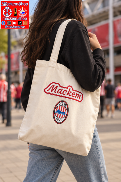 A person outdoors carrying a cream canvas tote bag with 'Mackem' in red script and the FTM European 1879 crest below it. The background shows a blurred street scene with people and stadium architecture. A MackemShop logo is visible on top left corner.