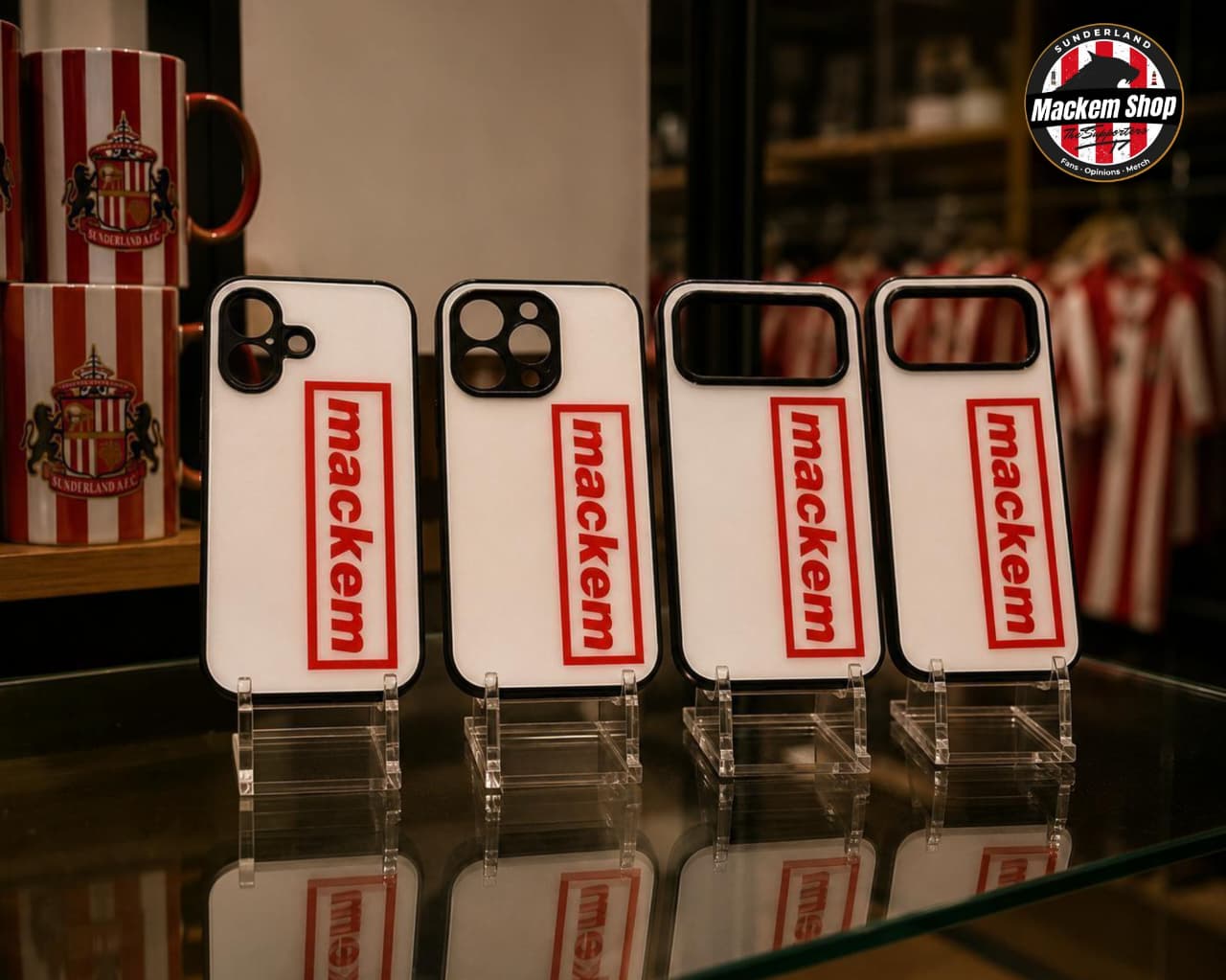 Four iPhone cases with 'mackem' branding on a reflective surface, with a blurred background.