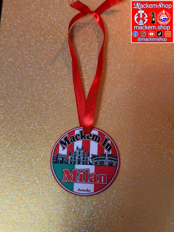 A round hanging ornament featuring the text 'Mackem In Milan' with a red ribbon loop at the top, shown on a glittery gold background. The ornament has a red, white, and green design with a black-and-white building illustration in the center. A MackemShop Logo is visible on top right corner.