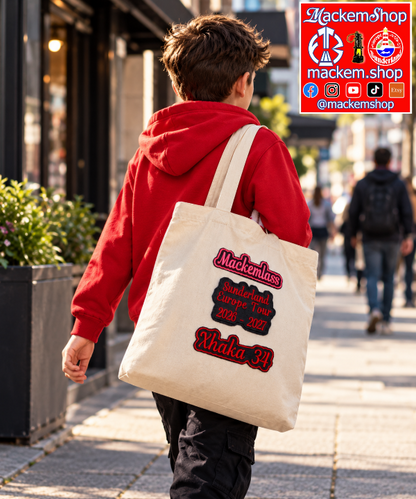 A Boy carrying a beige colour tote bag with patches of Mackemlass in Pink, Sunderland European tour 2026-27 in red on black, and Xhaka 34 in red on black, with a MackemShop logo visible on top right corner.