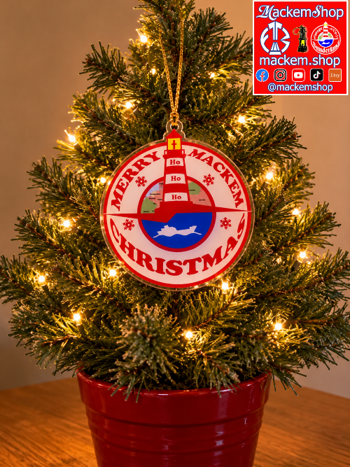 A festive round Christmas ornament hanging on a lit artificial Christmas tree in a red pot. The ornament is red and white with the words 'MERRY MACKEM CHRISTMAS' and a small illustration of a red house, white snowflakes, and a blue wave-like shape in the center. A MackemShop Logo is visible on top right corner.
