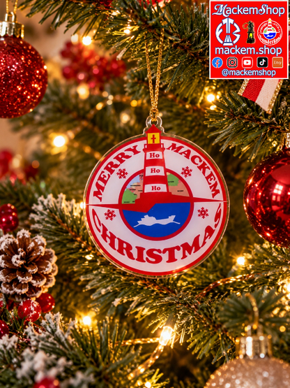 A round Christmas ornament hanging on a decorated tree, featuring a red and white lighthouse design with the text 'MERRY MACKEM CHRISTMAS' and a small boat in the center. The ornament is surrounded by red ornaments, pinecones, and warm string lights. A MackemShop Logo is visible on top right corner.