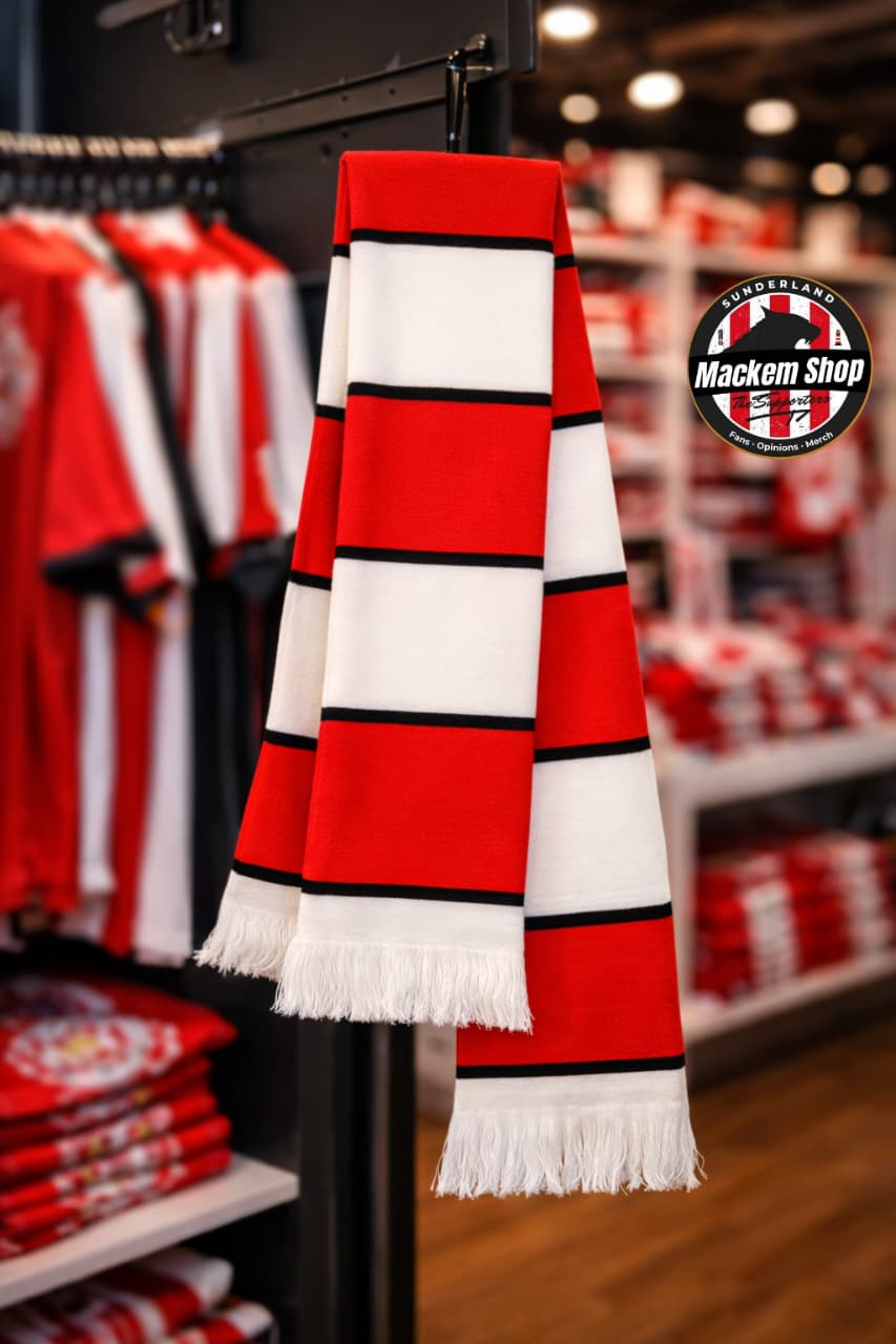 Red, white, and black striped scarf hanging in a store with sports merchandise in the background.