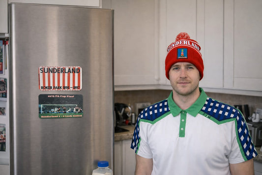 Person wearing a Sunderland Lighthouse Bobble Hat and A blue and white striped with green color polo shirt standing in a kitchen next to a refrigerator with magnets.