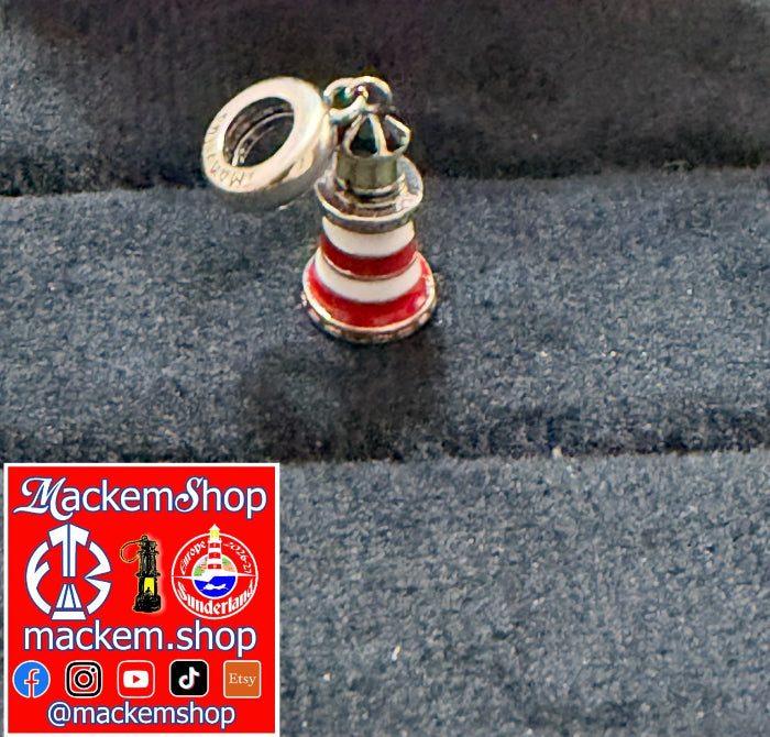 A Roker lighthouse-shaped charm with red, white, and silver detailing, shown on a dark textured fabric background. A red square watermark with the text 'MackemShop'.