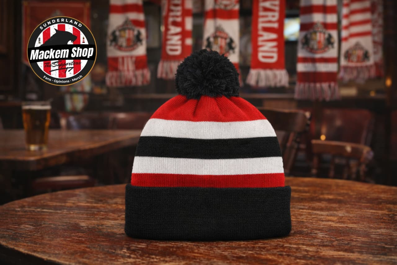 Roker Retro Bobble hat by Mackem shop placed on a wooden table in a bar with Sunderland Afc scarfs in background with a bear glass.