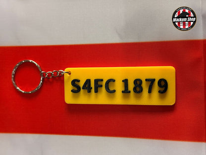 Yellow keychain with black text 'S4FC 1879' on a red and gray background
