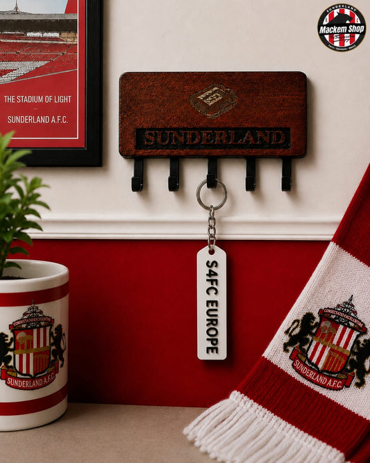 A wooden Sunderland AFC wall hook holder with black hanging loops, shown mounted on a wall above a red-and-white Sunderland mug and scarf. A white keychain tag reading 'S4FC EUROPE'.