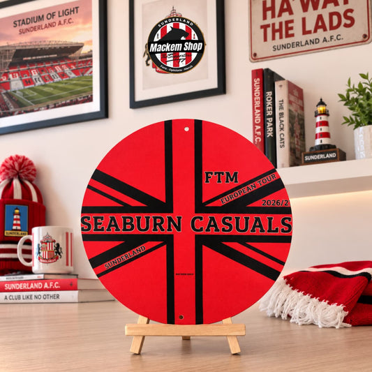 A circular red and black Seaburn Casuals FTM Metal sign on a small wooden easel stand, displayed on a tabletop with Sunderland-themed decor in the background.