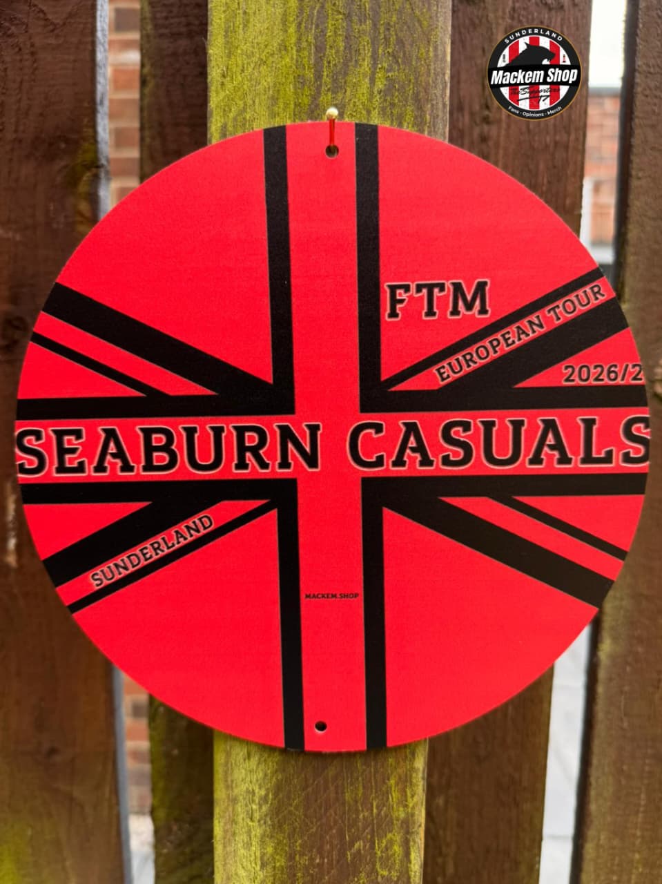 Circular red and black metal sign by MackemShop with 'Seaburn Casuals' branding on a wooden post.
