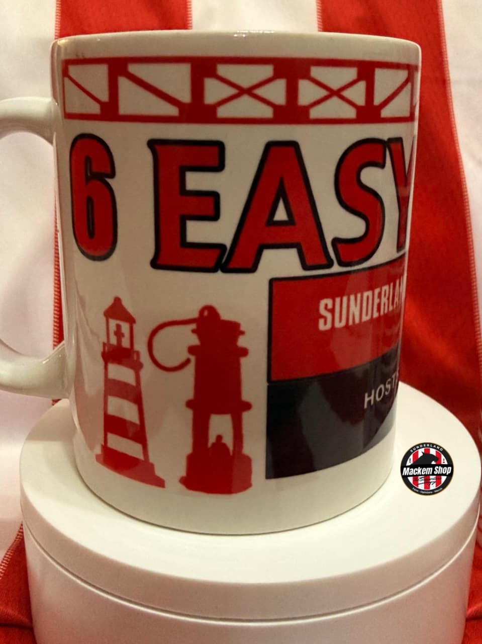 White mug with red and black text and graphics on a white stand with a red background