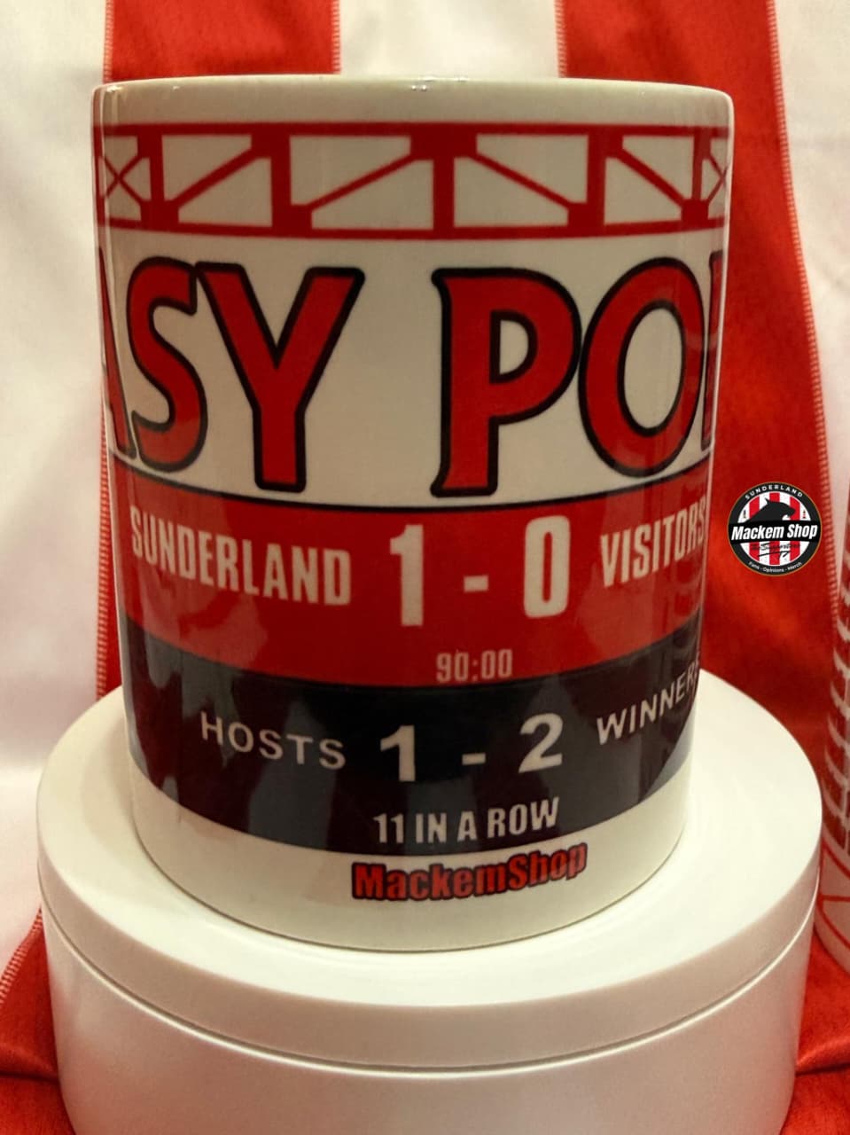 Mug with sports-themed design featuring text and graphics, placed on a white stand with a red background.