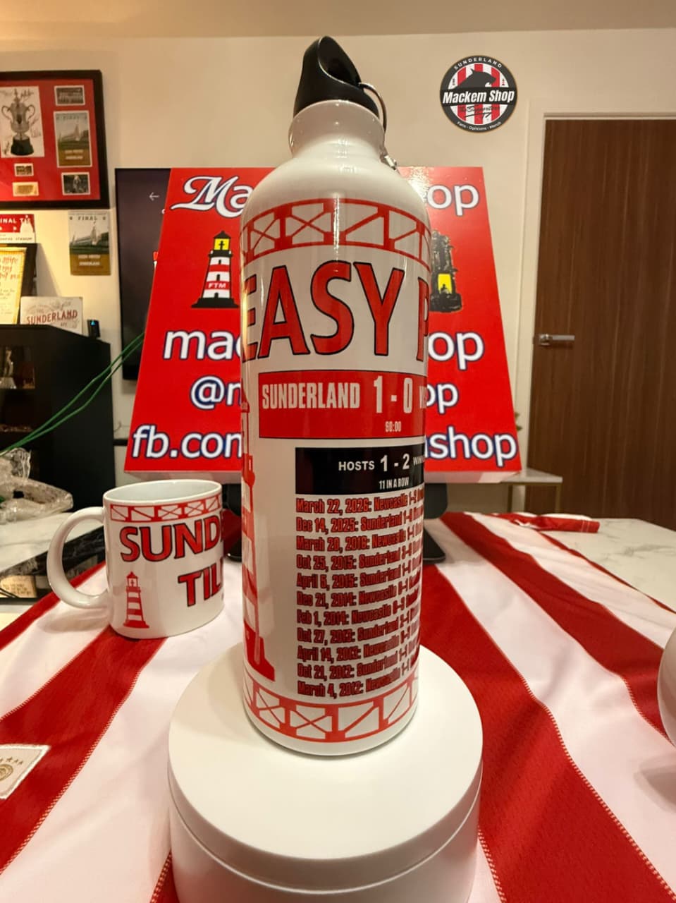 Large bottle labeled 'EASY' on a table with a red and white striped cloth, in front of promotional signs.
