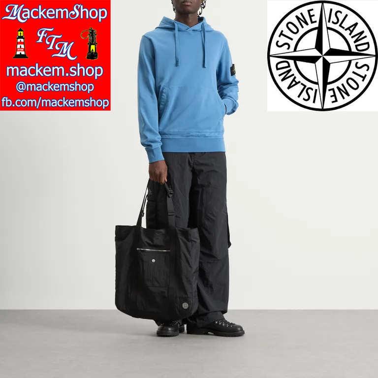 Person wearing a blue hoodie and black pants holding a black bag, with Stone Island logo and Mackem Shop branding.