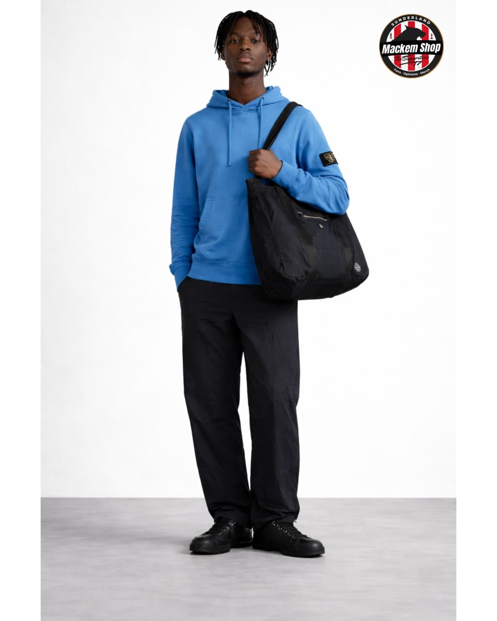 Person wearing a blue hoodie and black pants holding a black Tote bag on a white background