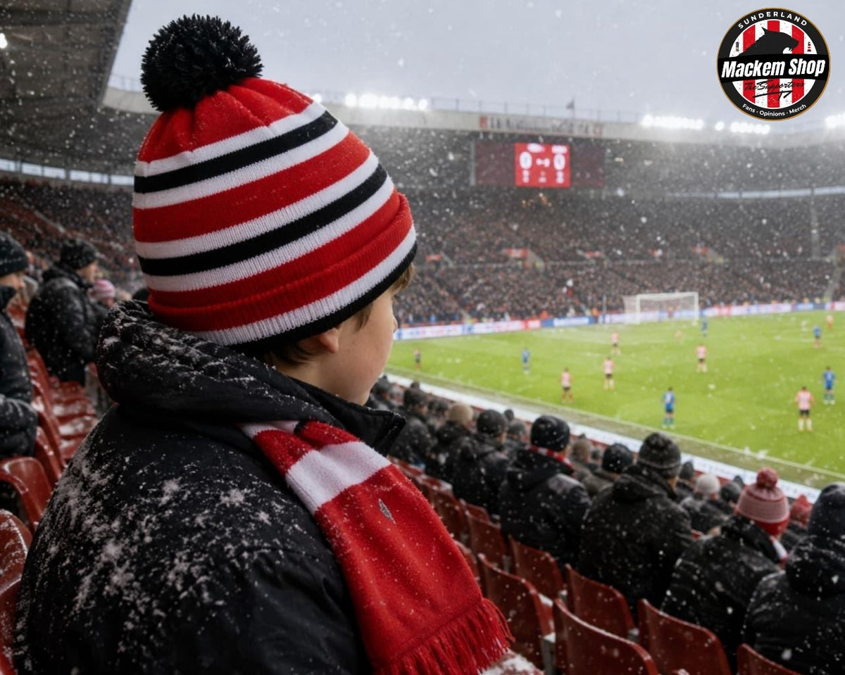 A person wearing a red, white, and black striped knit beanie with a black pom-pom and a matching red and white scarf, standing in a stadium during a snowstorm. The stadium crowd is visible in the background, and a 'Mackem Shop' logo is in the top right corner.
