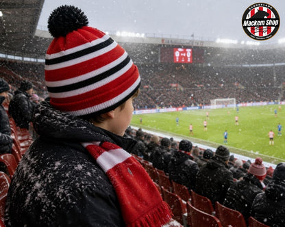 A person wearing a red, white, and black striped knit beanie with a black pom-pom and a matching red and white scarf, standing in a stadium during a snowstorm. The stadium crowd is visible in the background, and a 'Mackem Shop' logo is in the top right corner.