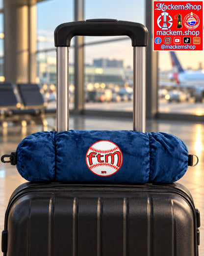 A navy-blue plush travel pillow with a red and white embroidered 'ftm baseball' logo, resting on top of a black hard-shell suitcase in an airport terminal, with MackemShop Logo.