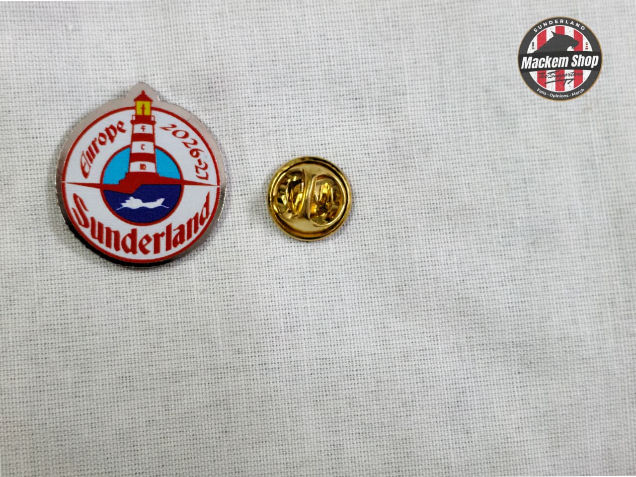 Two pins on a textured gray background, one with a lighthouse design and text, the other gold.