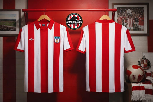 Two red and white vertically striped football jerseys hanging on wooden hangers against a red wall. The left jersey shows the front with a red collar, Umbro logo on the right chest, and a club crest on the left chest.