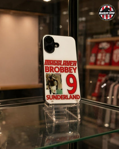 A white phone case featuring a red and black 'MaggSlayer Brobbey 9 Sunderland' design, displayed on a clear acrylic stand inside a glass display case with a blurred store background.