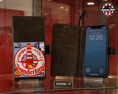A Black folio iPhone case with a colorful 'Europe 2025 Sunderland' graphic, shown in both closed and open states on a glass display shelf next to an iPhone 12.