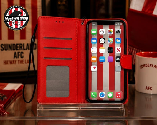 A red folio iPhone case with a vertical red-and-white striped pattern on the interior flap, shown open with a smartphone inserted. The case has card slots, a clear ID window, and a wrist strap, photographed on a reflective surface.