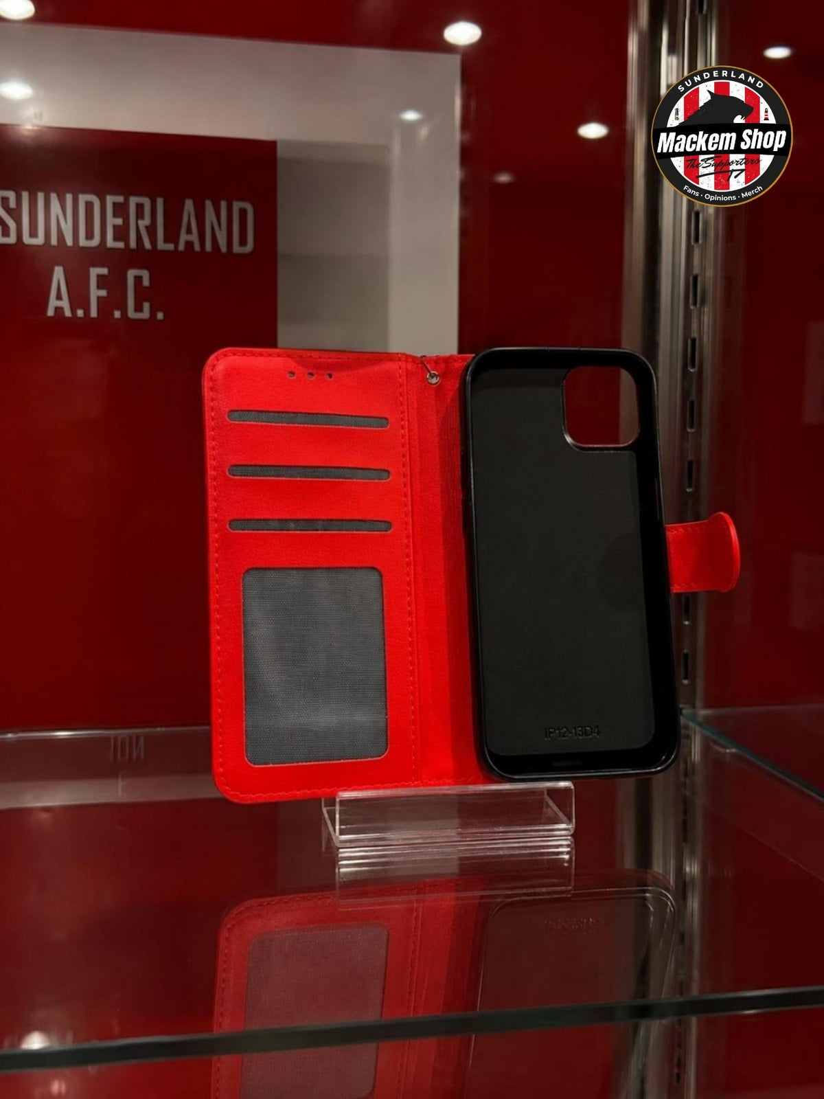 A red folio-style iPhone case shown open on a glass display stand. The case has card slots and a clear ID window on the inside.