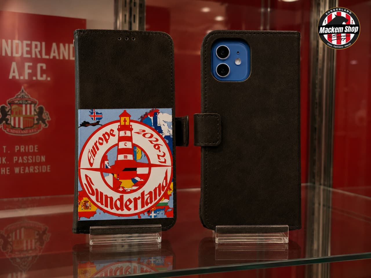 Two Black flip iPhone 12 cases displayed on a glass shelf. The left case features a large Sunderland AFC graphic with the 'Europe 2026-27' text, and a lighthouse illustration.