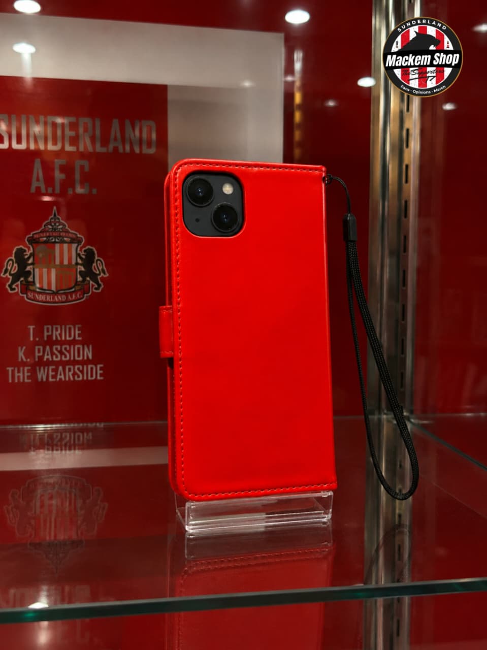 A bright red leather iPhone case with a black wrist strap, displayed on a clear stand inside a glass case.