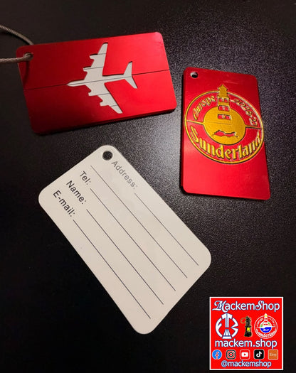 Three luggage tags on a dark textured surface: a red rectangular tag with a white airplane silhouette, a red rectangular tag with a gold circular Sunderland emblem, and a white rectangular address tag with printed fields. A Mackemshop logo appears in the bottom right corner.