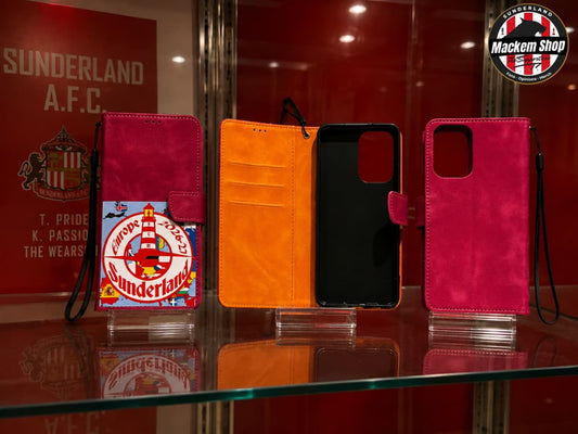 Red Samsung A53 phone wallet cases displayed on a glass shelf in a red showroom. One case is closed in magenta pink with a Sunderland Europe tour 2026-27 on it.