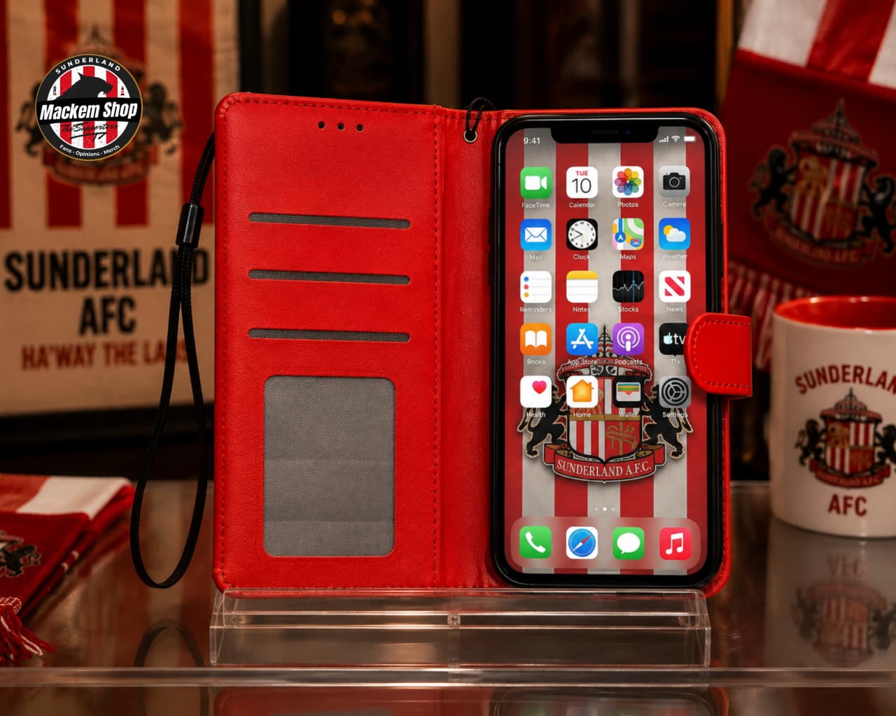 A red folio-style iPhone case with a black wrist strap, shown open with an iPhone inside. The case has card slots on the back and a small transparent window.