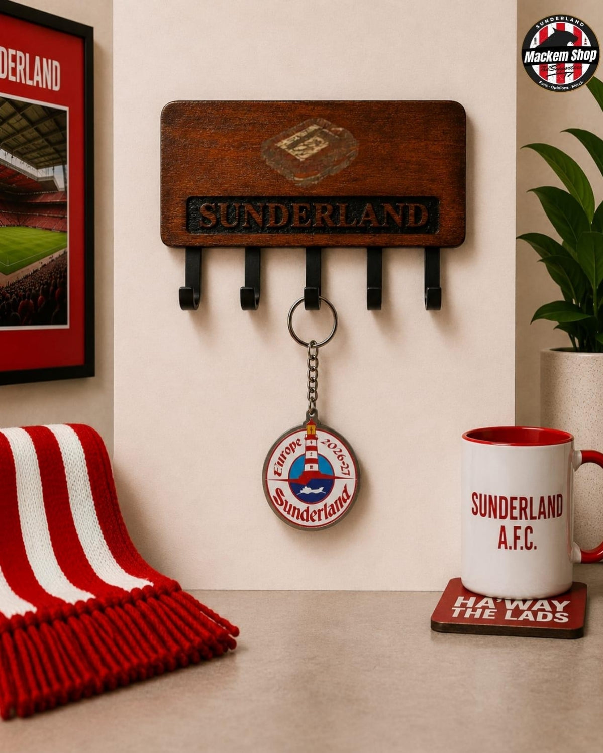 A wooden Sunderland AFC wall-mounted key holder with five black hooks, shown in a styled room setting with a red and white striped scarf, a framed picture, a plant, and a Sunderland A.F.