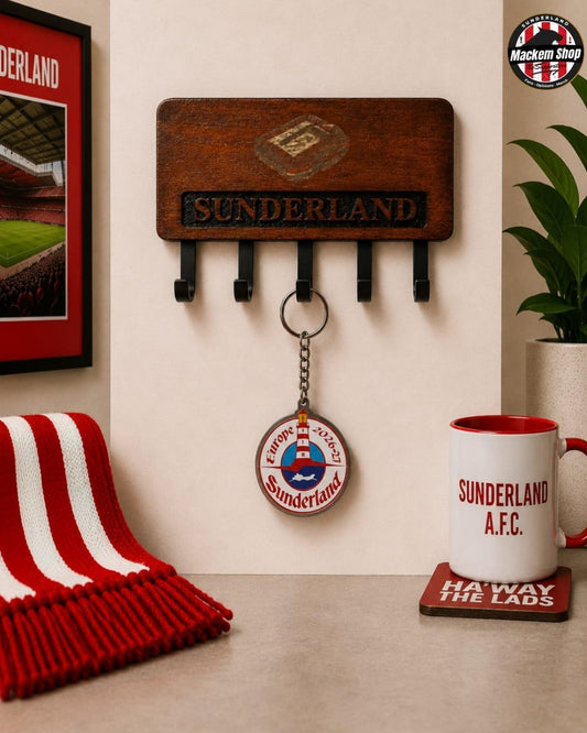A wooden Sunderland AFC wall-mounted key holder with five black hooks, shown in a styled room setting with a red and white striped scarf, a framed picture, a plant, and a Sunderland A.F.