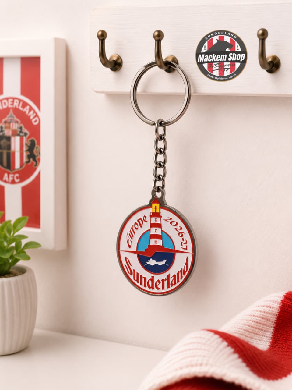 Keychain with Sunderland Europe 26/27 tour on a hook with a plant and red and white item in the background