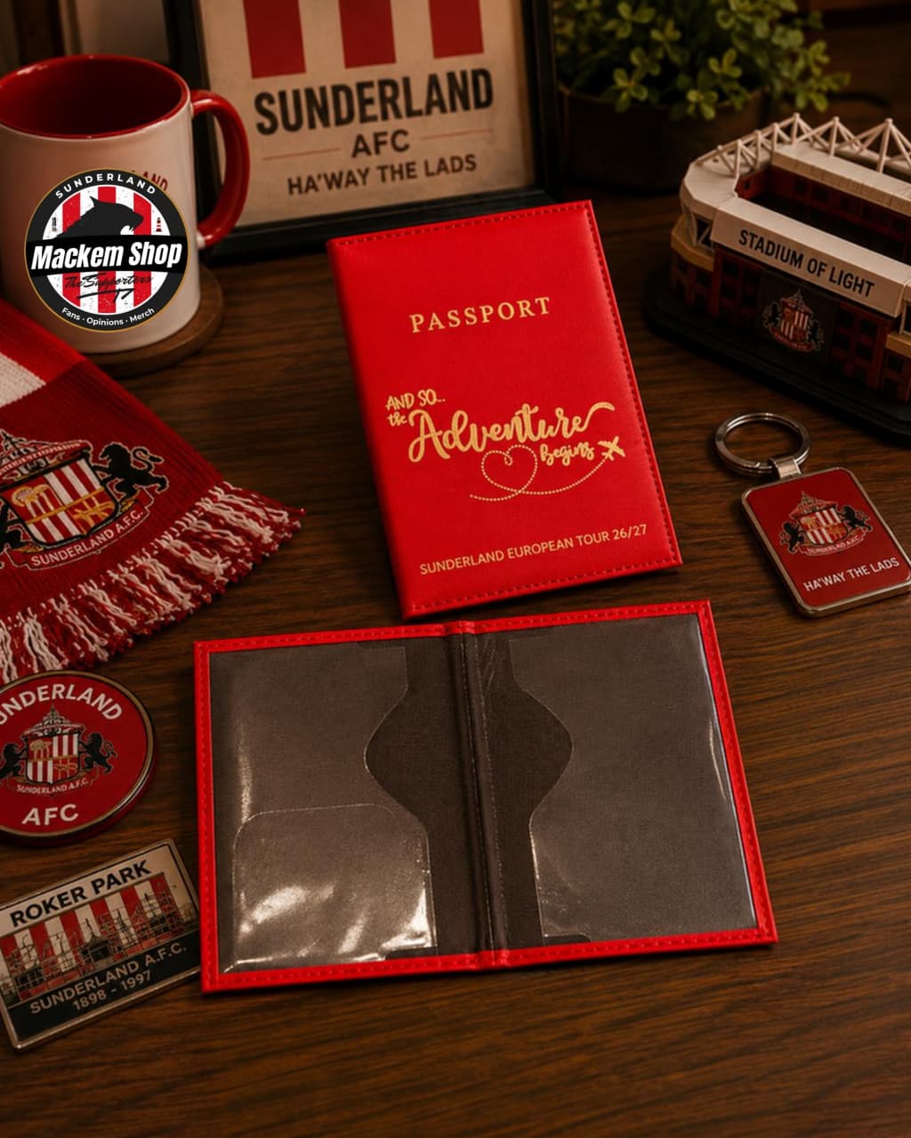 A red Sunderland AFC passport holder set displayed on a wooden table, including a red passport-style holder, a matching red scarf, a mug, a small stadium model, and a keychain, all branded with Sunderland AFC.