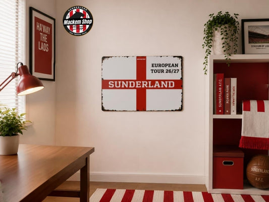 A rectangular vintage-style Sunderland football club sign with a red St George's cross on a distressed white background, hanging on a beige wall in a styled room with a desk, lamp, shelf, and plants.