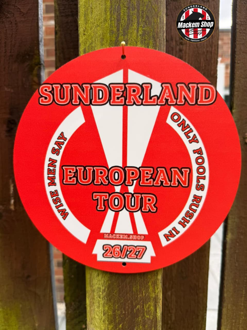 Circular red and white metal sign with text 'Sunderland European Tour' on a wooden post.