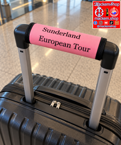 A black hard-shell suitcase with an extended telescoping handle, featuring a bright pink handle wrap printed with 'Sunderland European Tour' in black text. The suitcase is photographed on a polished tiled floor in an airport or train station setting. A MackemShop Logo is visible on top right corner.