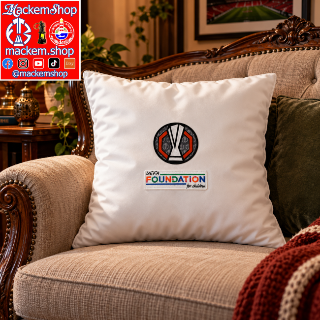 A square white throw pillow featuring a UEFA Foundation for Children logo, displayed on a beige upholstered armchair in a living room setting. A Logo for 'MackemShop' is visible in the top-left corner.
