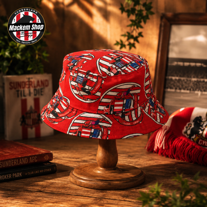 Red bucket hat with pattern on a wooden stand, surrounded by books and a flag, with 'Mackem Shop' logo.
