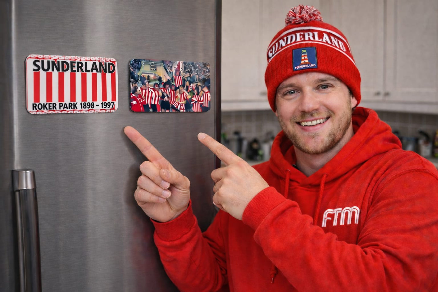 Person in red FTM Hoodie by Mackem Shop pointing at Sunderland-themed magnets on a refrigerator